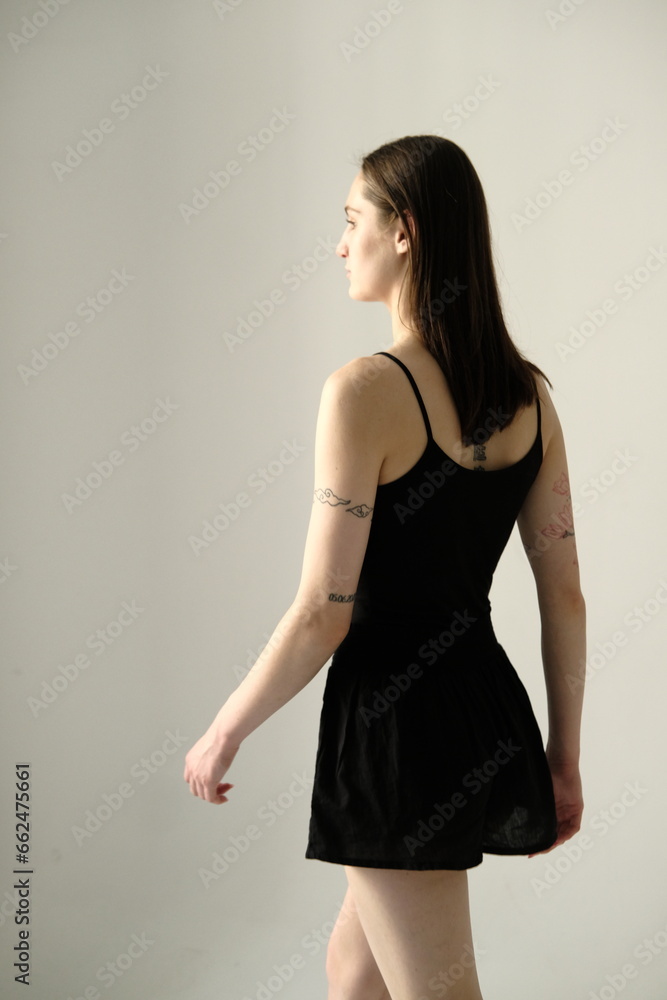 Portrait of a brunette girl without make up on a grey backgroung in a black summer clothes. Back view Portrait of a brunette girl without make up on a grey backgroung in a black summer clothes. Back view