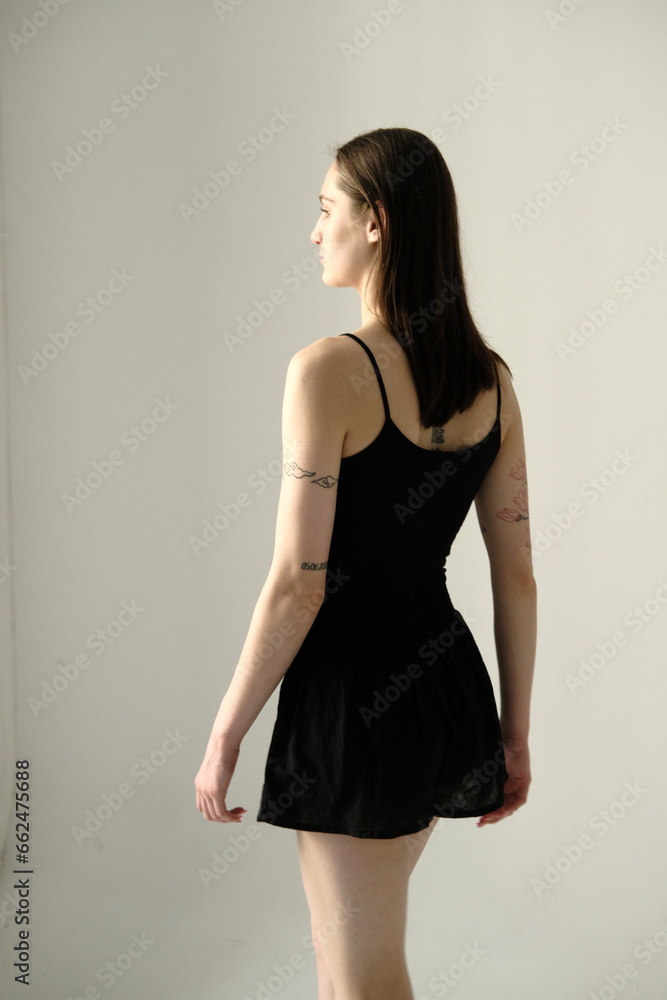 Portrait of a brunette girl without make up on a grey backgroung in a black summer clothes. Back view Portrait of a brunette girl without make up on a grey backgroung in a black summer clothes. Back view