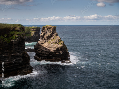 Rough stone cliffs and blue Atlantic ocean surface with waves. Ireland, Kilkee area. travel, tourism and sightseeing concept. Irish landscape and coastline. Warm sunny day.