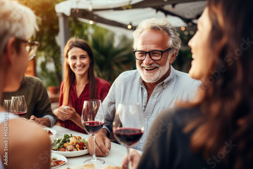 Happy family dining and tasting red wine glasses in barbecue dinner party - People with different ages and ethnicity having fun together - Youth and elderly parents and food weekend activities photo