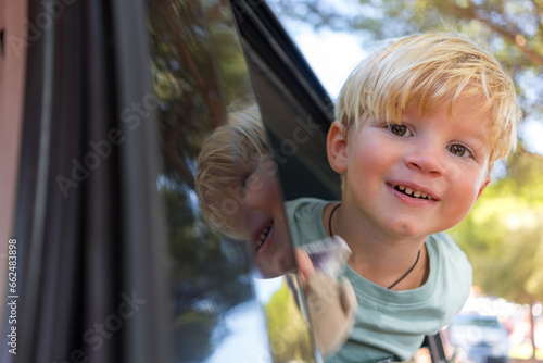 a little blond boy of three years old looks out of the car window and smiles