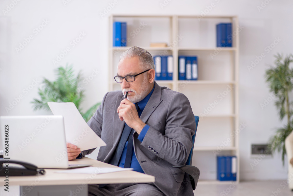Old male employee reading paper at workplace Old male employee reading paper at workplace