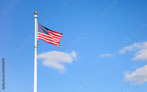 US flag waving in the wind against a blue sky. Symbol of freedom, unity, and national pride. Perfect for patriotic themes