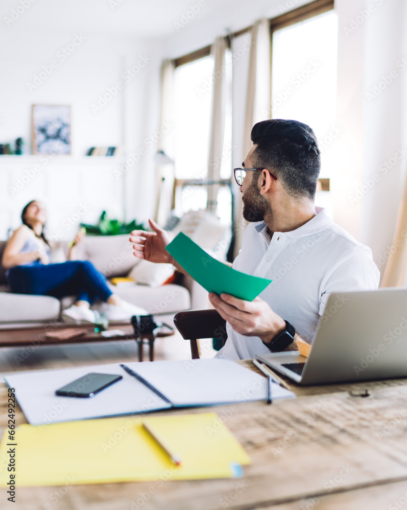 Dark haired and bearded man asking woman sitting on sofa to come up Dark haired and bearded man asking woman sitting on sofa to come up