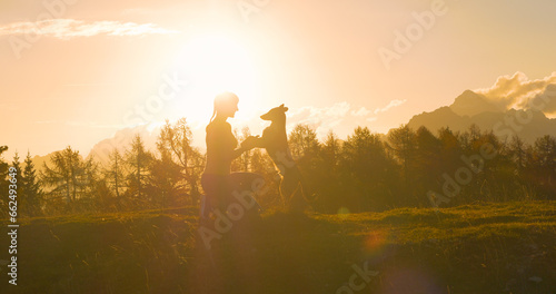 SILHOUETTE, LENS FLARE: Happy young lady on a mountaintop with her dog at sunset photo