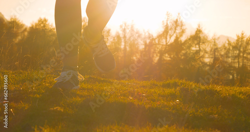 CLOSE UP  LENS FLARE Female feet running on golden glowing grassy mountain trail