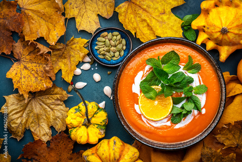 Sweet autumn pumpkin soup with cream, tangerine and mint. Winter healthy vegetarian comfort slow food. Soup bowl on green table background. Top view