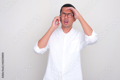 Adult Asian man showing stress expression when answering a phone call photo