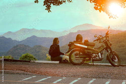 woman sitting beside motorcycle at beautiful viewpoint and looking to sunset scene