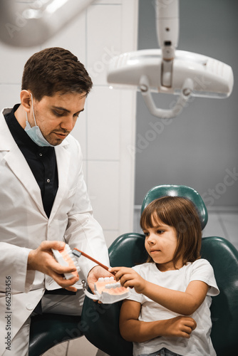 A dentist on a jaw model teaches a child girl to brush teeth.