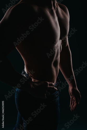 Stunning and well-built man standing in a dark room and posing