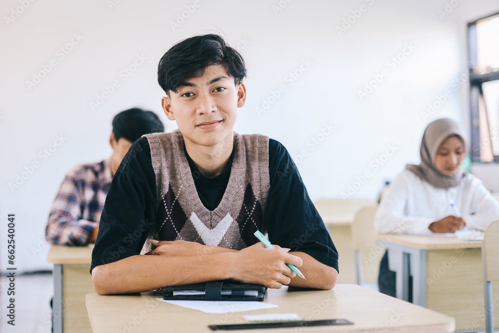 Portrait of smiling asian male student sitting at desk in classroom at university Portrait of smiling asian male student sitting at desk in classroom at university