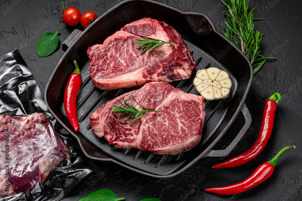 Raw organic marbled beef steaks with spices on a wooden cutting board on a black slate, stone or concrete background.