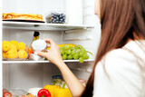 Woman hand taking, grabbing or picks up camembert or brie cheese out of open refrigerator shelf, fridge drawer full of fruits, vegetables, banana, peaches, yogurt. Healthy food diet, lifestyle concept