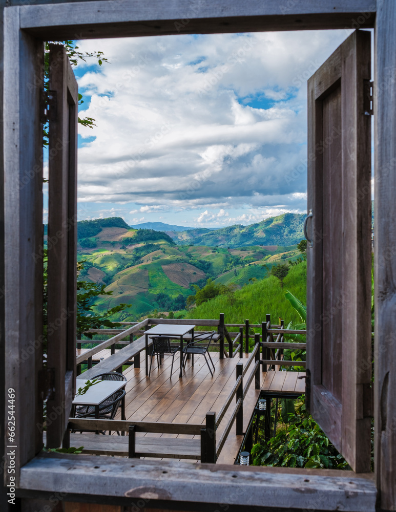 Fototapeta premium a view trough a wooden window at the green mountains of Doi Chang Mountains of Chiang Rai Northern Thailand, Natural mountain view on Doi Chang, Chiang Rai Province, Thailand