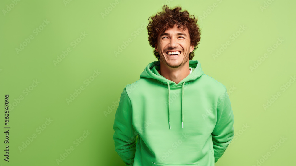 Ultra handsome man with curly hair, smiling and laughing, wearing a solid deep green sweatshirt. deep solid green background similar to the dress color. Ultra handsome man with curly hair, smiling and laughing, wearing a solid deep green sweatshirt. deep solid green background similar to the dress color.