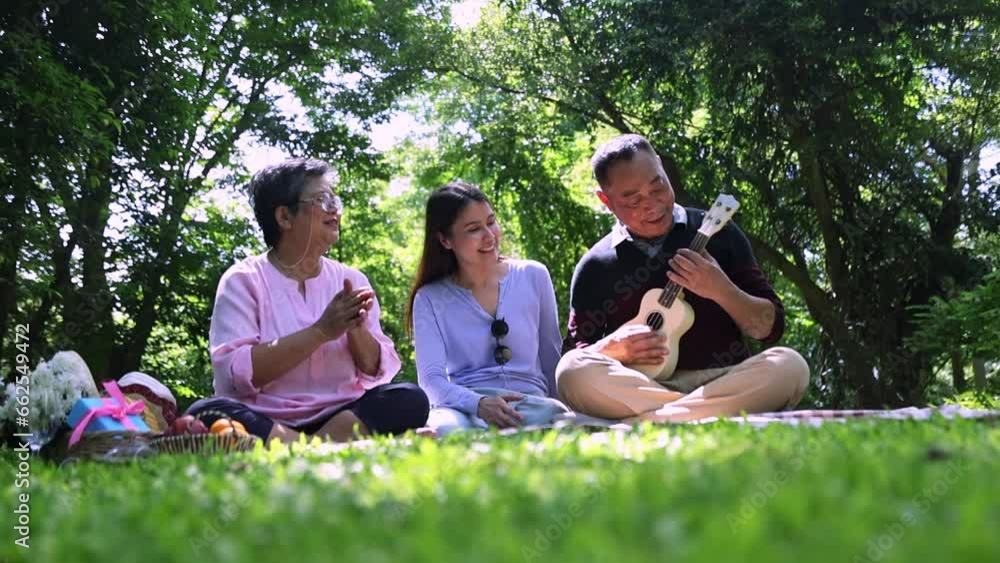 Happy asian family traveling doing picnic activities taking care their health sitting playing ukulele singing applauding mother and father sitting together daughter supporting family relationship. Happy asian family traveling doing picnic activities taking care their health sitting playing ukulele singing applauding mother and father sitting together daughter supporting family relationship.