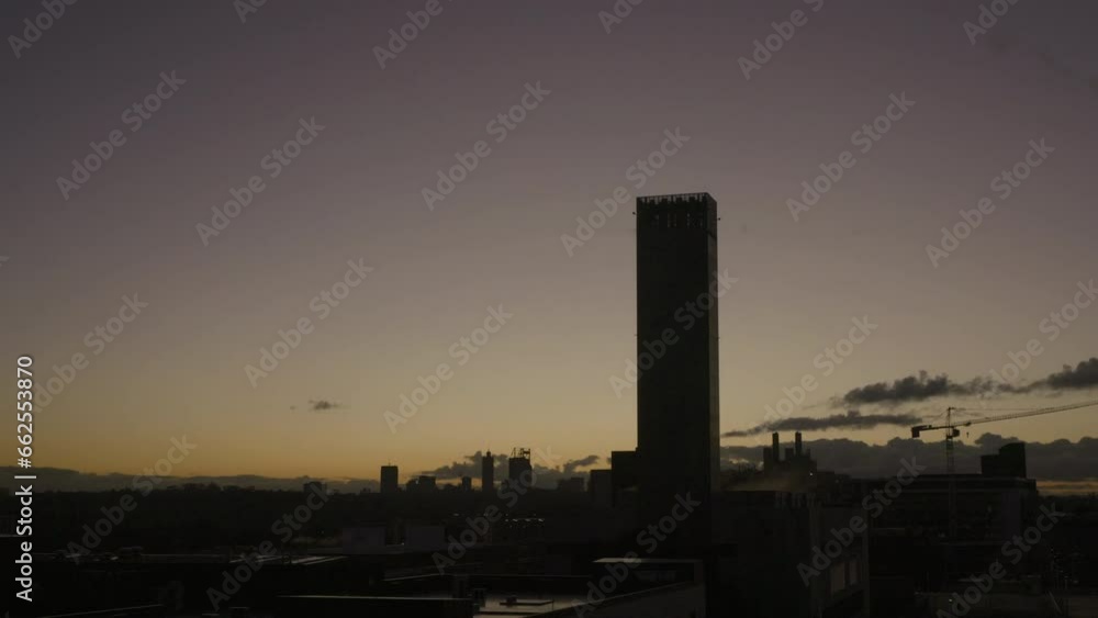 Dawn to sunrise over city dominated by a single high-rise building. New moon ascends above orange hues. As sun emerges in cloudless sky a crane begins to swing heralding the new day. Timelapse Dawn to sunrise over city dominated by a single high-rise building. New moon ascends above orange hues. As sun emerges in cloudless sky a crane begins to swing heralding the new day. Timelapse