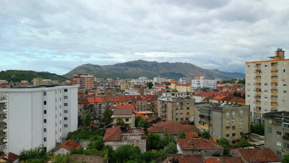 Aerial drone tilt up shot over city buildings with mountains in the background in Shkodra, also known as Shkoder or Scutari along the northwestern Albania. Aerial drone tilt up shot over city buildings with mountains in the background in Shkodra, also known as Shkoder or Scutari along the northwestern Albania.