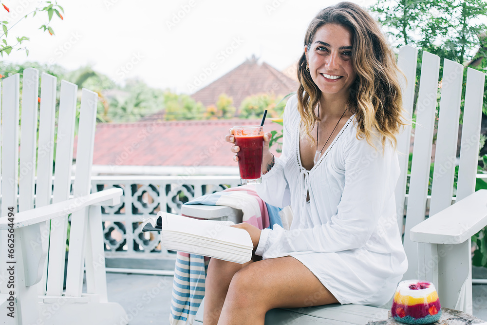 Pleased adult woman reading book and drinking red juice on terrace Pleased adult woman reading book and drinking red juice on terrace