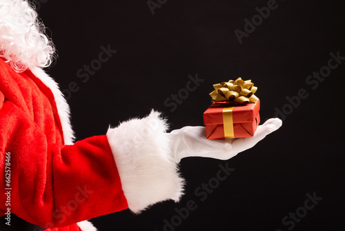 Santa claus holding red christmas present with copy space on black background