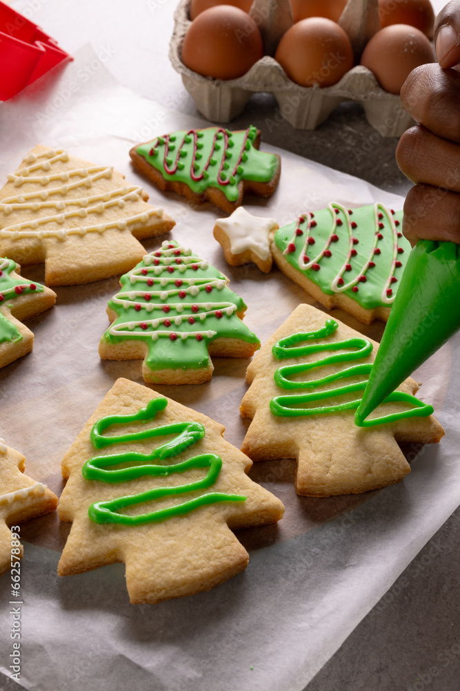 Vertical image of african american woman's hand decorating christmas cookies with copy space