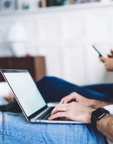 Adult man working at laptop while sitting near woman