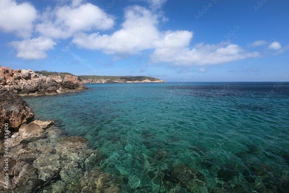 Picturesque sandy beach with crystal-clear blue waters and rocky shoreline in  Ibiza