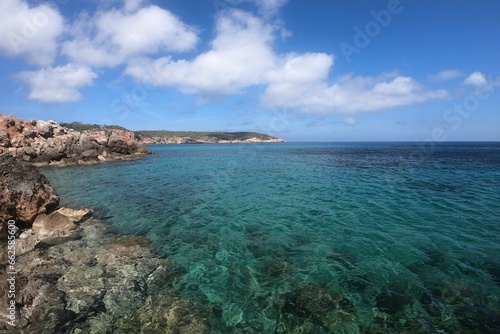 Picturesque sandy beach with crystal-clear blue waters and rocky shoreline in Ibiza