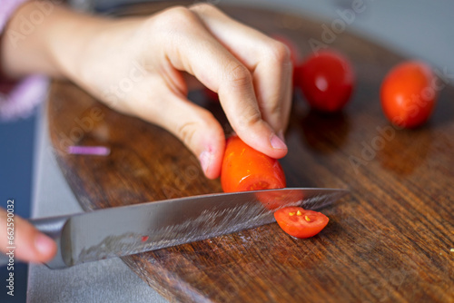 child's hand cuts a cherry tomato into slices on a cutting board
