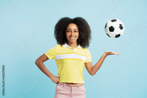 Confident African American woman with curly hair holding soccer ball looking at camera © Maria Vitkovska