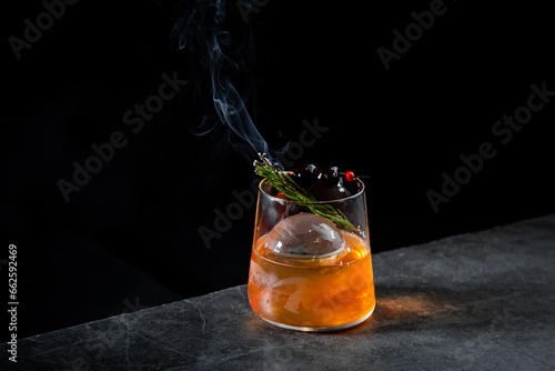 aromatic cocktail with a sprig of pine needles and round ice on a dark background, side view