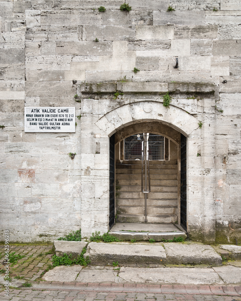 Arched entrance with open green metal door in brick stone wall leading to 16th century Atik Valide Mosque in Uskudar district, Istanbul, Turkey