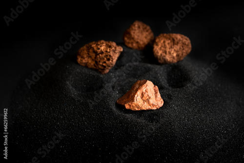 Lumps of pure copper or pink gold ore on a black sand background photo