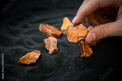 Man's hand holding a piece of copper to examine it for industrial use on black background
