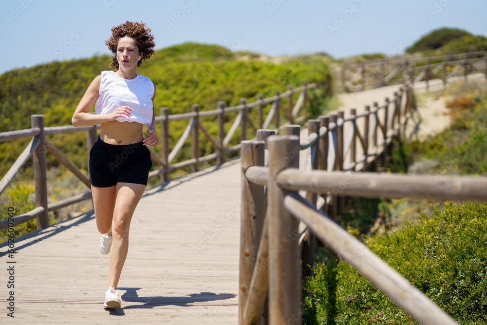 Sportive woman running along walkway in countryside