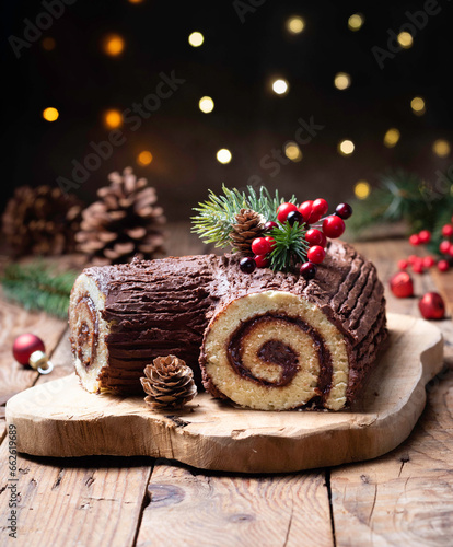 Close-up of a Christmas chocolate yule log (Buche de Noel) on a wooden chopping board with festive berry, pinecone and fir branch decorations