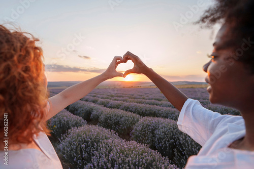 Friends showing heart sign amidst lavender field photo