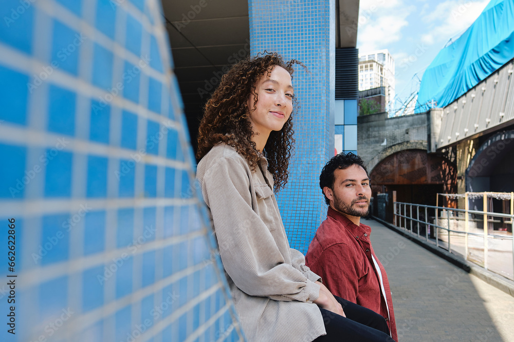 Smiling man with woman sitting on wall at footpath Smiling man with woman sitting on wall at footpath