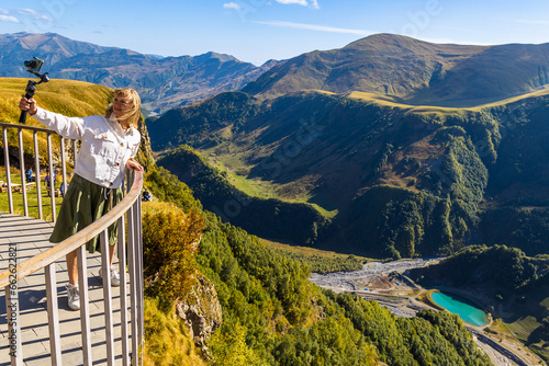 A girl stands on the observation deck of the Arch of Friendship of Peoples and takes a selfie against the backdrop of a picturesque mountain landscape. Georgia, Caucasus photo