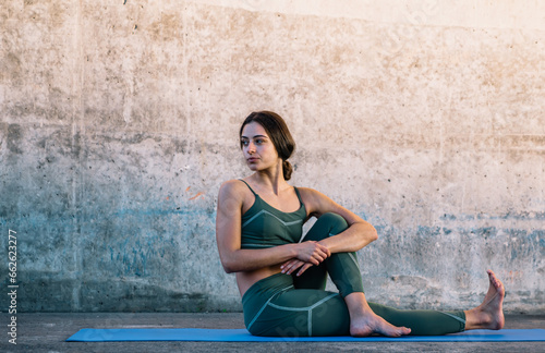 Young woman making yoga pose while sitting on fitness mat