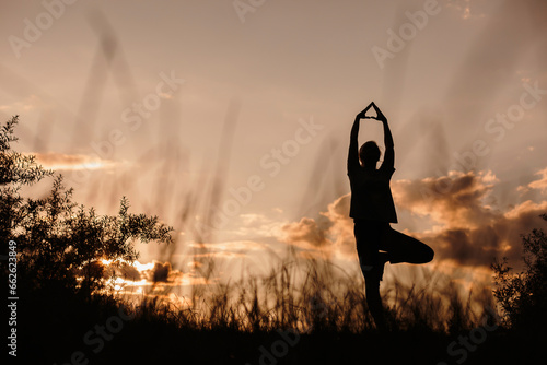 Silhouette woman practicing tree pose yoga at sunset photo