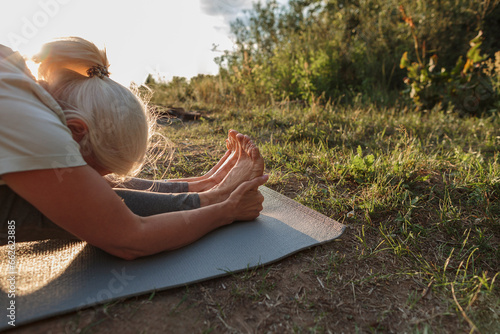 Mature woman practicing yoga on mat at sunset photo