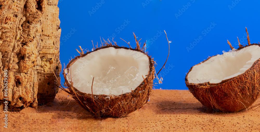 Fresh coconut split in half and resting in the sand with a liquid splash.