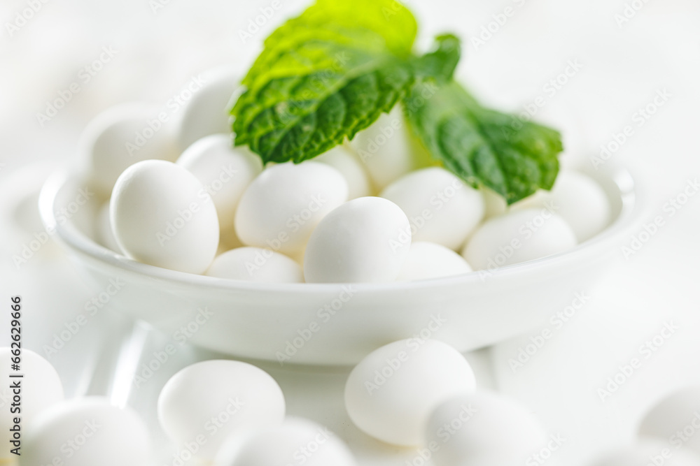 Mint candies in bowl. Menthol bonbons and mint leaves on white table. Mint candies in bowl. Menthol bonbons and mint leaves on white table.
