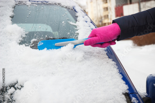 Hand of woman using brush and remove snow from car and windscreen