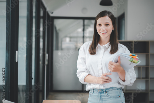 Successful businesswoman standing in creative office and looking on camera. Woman entrepreneur in a coworking space smiling..