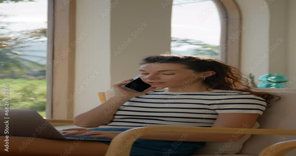 Young woman using laptop computer and a smartphone while sitting in armchair at home. Freelance concept Young woman using laptop computer and a smartphone while sitting in armchair at home. Freelance concept