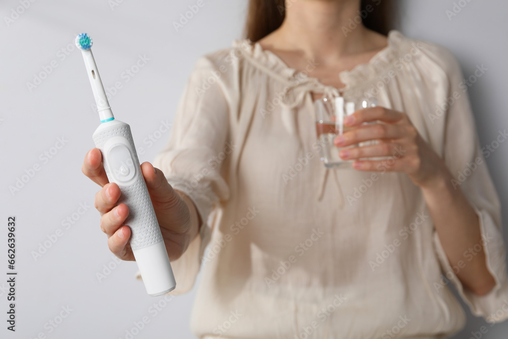 Electric toothbrush and glass in female hands on white background Electric toothbrush and glass in female hands on white background