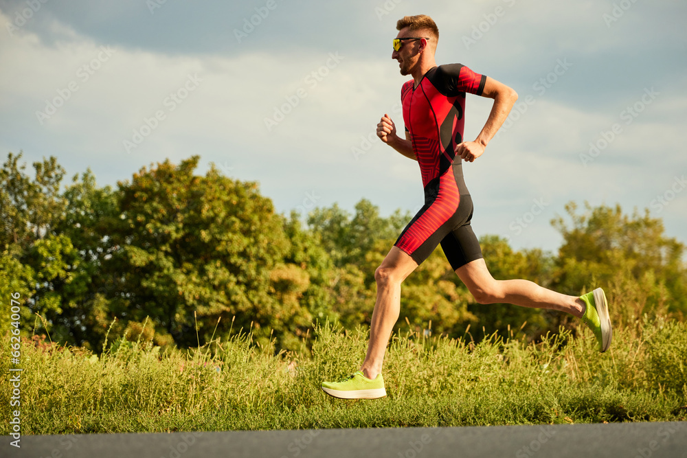 Dynamic image of competitive man in sportswear, athlete training outdoors on summer day, running. Marathon. Concept of professional sport, triathlon preparation, competition, athleticism Dynamic image of competitive man in sportswear, athlete training outdoors on summer day, running. Marathon. Concept of professional sport, triathlon preparation, competition, athleticism